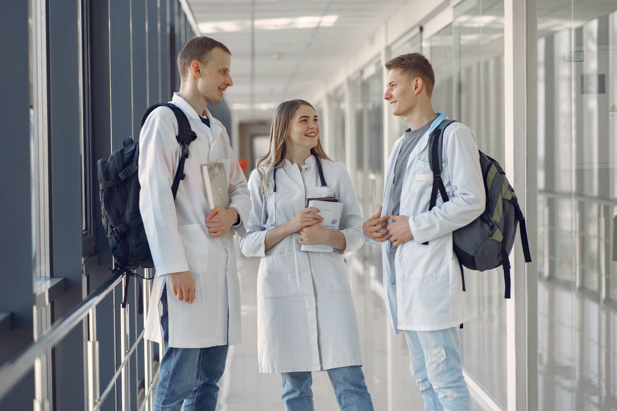 Three medical students in white coats talking together in a corridor